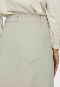 Lichtgrijze denimrok met een aansluitende taille, twee achterzakken en subtiele stikdetails. Gladde textuur met een schone, minimalistische uitstraling.