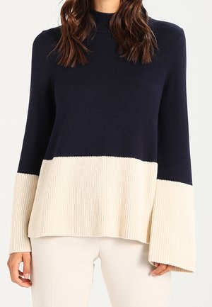 Sweter w kolorze granatowym i kremowym, z blokowaniem kolorów, o prążkowanej strukturze, wysokim kołnierzu i szerokich rękawach, charakteryzujący się luźnym, swobodnym krojem.