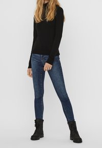Musta pitkähihaisen neuleen yhdistelmä tummansiniset skinny-farkut ja mustat nauhalla varustetut nilkkurit. Sujuva kangas ja istuva malli.