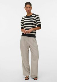 Maglione a righe in nero e crema, maniche corte, scollo a costine, abbinato a pantaloni beige chiaro, completato con sandali con tacco neri.