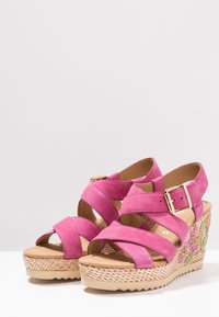 Sandali con zeppa in suede rosa, con cinturini incrociati, fibbia regolabile e suola intrecciata testurizzata con dettagli ricamati colorati.