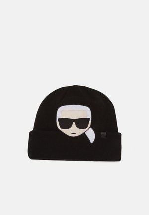 Bonnet en tricot noir avec un visage stylisé présentant des cheveux blancs, des lunettes de soleil noires et une queue de cheval latérale brodée sur le devant.