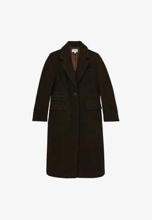 Femme portant un blazer marron foncé à motif pied-de-poule sur une chemise foncée boutonnée, montrant le haut du torse et les épaules.