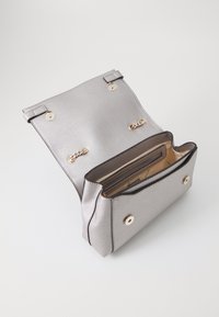 Bolso cruzado metálico plateado con una superficie texturizada, herrajes en tono dorado, dos cierres magnéticos y compartimentos para tarjetas en el interior.