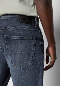 Mörkblå denimjeans med rak passform, utrustade med en läderetikett i midjan och kontrasterande sömmar. Bakfickor formade med en liten logotyp.