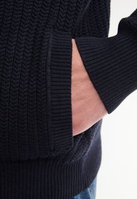 Marineblauw gebreid sweater met textuur, voorzien van geribbelde manchetten en een zak, met een geweven patroon en een zachte stofafwerking.