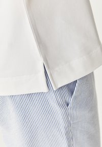 White cotton t-shirt with side slits, paired with blue and white striped fabric pants featuring a textured pattern and side pocket.