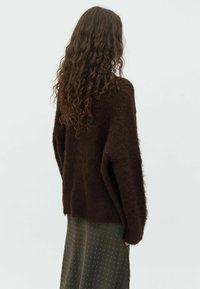 Brown fluffy sweater with a loose fit, paired with a green patterned skirt. The texture is soft, featuring a high neckline and drop shoulders.