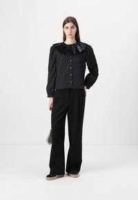 Svart bluse med en stor volangkrage, pyntet med blanke detaljer og knappelukking. Kombinert med svarte vide bukser og sneakers.