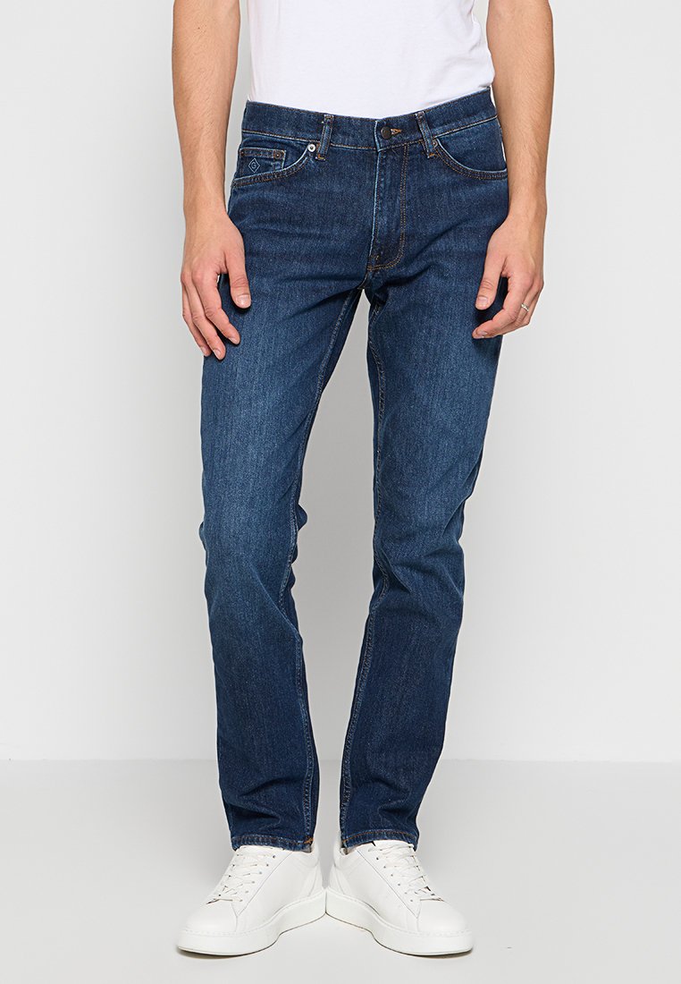 Granatowe dżinsy o prostym kroju, z pięcioma kieszeniami, pomarańczowymi szwami i zapinane na zamek, połączone z białymi snekerami.