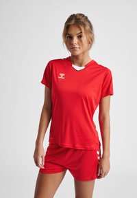 Rød træningsskjorte og matchende shorts lavet af letvægtigt stof. Skjorten har rund halsudskæring, korte ærmer og et logo på brystet.