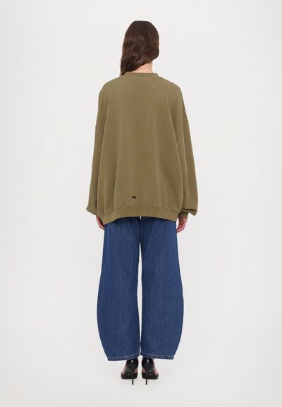 Overdimensioneret olivengrøn sweatshirt med rund halsudskæring, parret med brede blå denimjeans. Blødt materiale, minimalistikke detaljer.