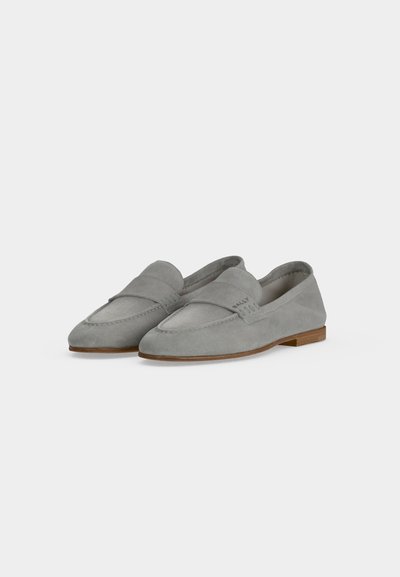 Paire de mocassins en daim gris clair avec petits talons en bois et bande décorative sur le dessus, sur un fond blanc uni.