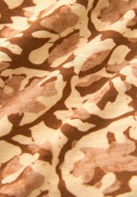 Katoenen stof met een beige achtergrond en abstracte bruine luipaardprint, die een zachte textuur en een mix van ronde en hoekige vormen laat zien.