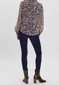 Läpinäkyvä, kukkakuosinen pusero violettina, vihreänä ja vaaleanpunaisena, yhdistetty tummansinisiin kapealahkeisiin farkkuihin ja kiiltäviin ruskeisiin nilkkureihin, joissa on tukeva korko.