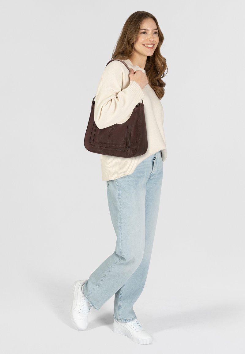 Borsa a spalla in pelle marrone con finitura testurizzata, dotata di una tracolla larga e un motivo cucito distintivo, tenuta da una persona che indossa un maglione chiaro.
