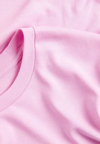 Lyserøde bomulds-t-shirts med ribbet rund hals, blød tekstur og glat stof, let krøllede og ligger oven på hinanden.
