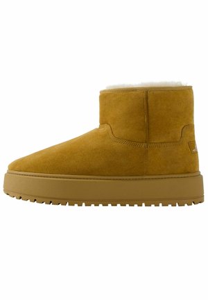 Bottine en suède jaune avec une douce doublure en fourrure blanche, une semelle en caoutchouc plate et des détails de couture minimaux. Design simple et arrondi.