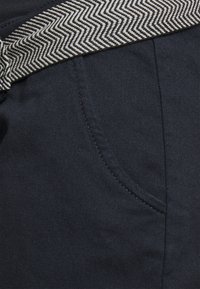 Námořnické modré kalhoty se páskem s vzorem herringbone. Obsahují přední kapsu s kontrastním stehem. Odolná látka s vroubkovanou texturou.