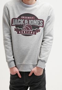 Sudadera gris de mezcla de algodón con cuello redondo, puños de canalé y un gráfico frontal que presenta el texto "JACK & JONES" y "HUNTERS".