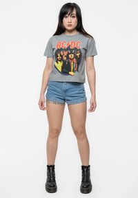 Gray cropped t-shirt featuring AC/DC graphic, paired with light blue denim shorts and black lace-up combat boots. Simple, casual design.