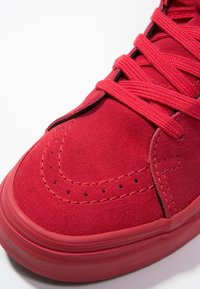 Zapatillas de ante rojo con cordones planos, puntera lisa, detalles de costura y una suela de goma con un patrón texturizado.