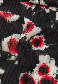 Tissu noir avec une texture froissée, ornée de motifs floraux rouges et blancs, créant un effet visuel contrasté et superposé.