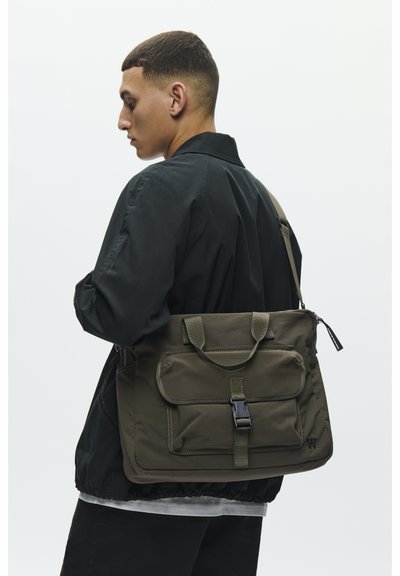 Sac messager vert olive avec rabat, poche avant et sangle réglable. Fabriqué en tissu durable avec une finition texturée et des accessoires noirs.