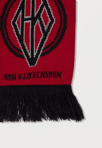 Rdeč šal s črnimi cofki, ki prikazuje geometrijski vzorec v črni in sivi barvi, s stiliziranim črko "H" in napisom "HAN HJØBENHAUN."