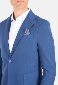 Blazer blu con texture, dotato di revers a punta, presenta una tasca sul petto con un fazzoletto a pois e un accento rosso sul revers.
