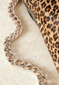 Leopardprint clutch bag met een goudkleurige metalen kettingriem. De tas heeft een gestructureerd oppervlak en een ritsluiting langs de rand.