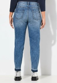 Faded blue denim jeans with five pockets, a high waist, tapered legs, and a cuffed hem. Back view showcases the stitching and pocket design.
