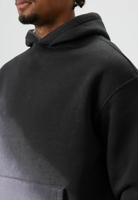 Zwarte hoodie met een gladde textuur, voorzien van een capuchon met trekkoord en een voorvak. Het ontwerp bevat een verloop naar lichtere tinten.