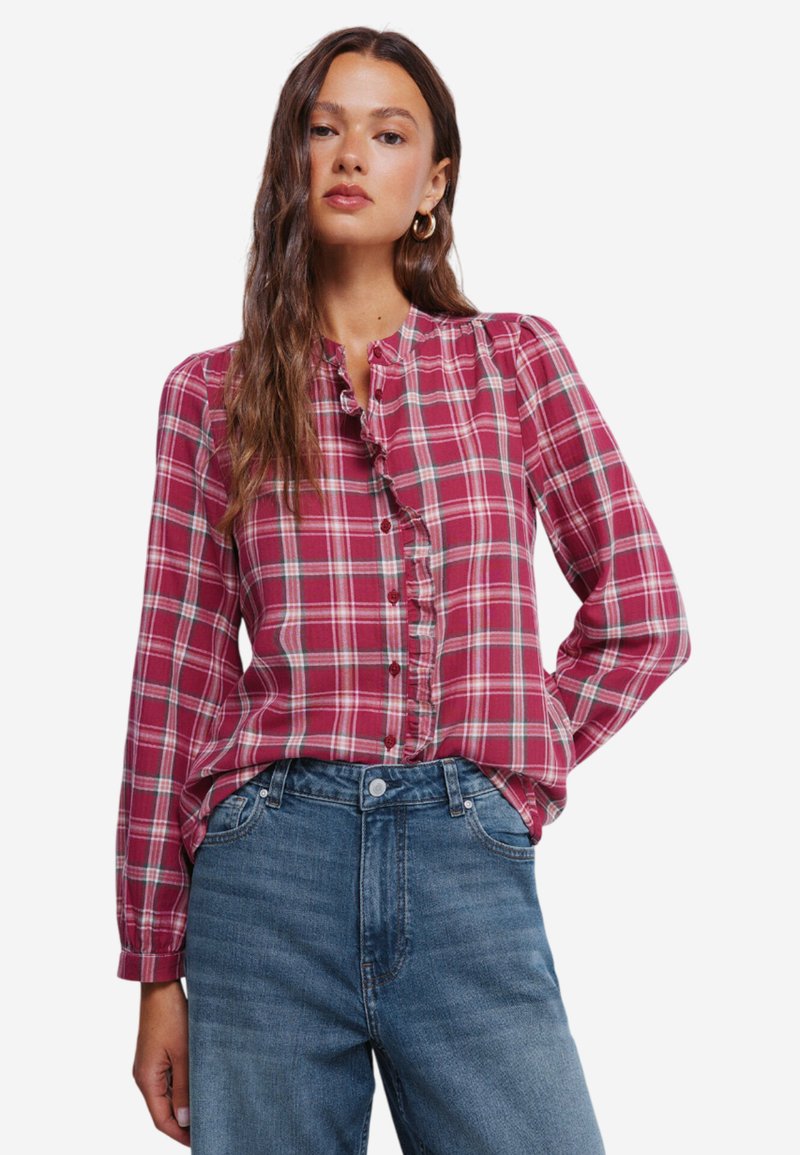 Rød og creme ternet skjorte med flæse-detalje langs knaplisten, lange ærmer og lige søm, båret med blå jeans.