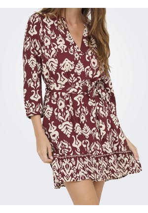 Femme portant une robe bordeaux avec un motif abstrait blanc, manches trois-quarts, encolure en V, taille nouée et ourlet à volants.