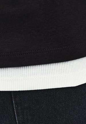 Zwarte katoenen T-shirt gelaagd over een witte geribde zoom, gecombineerd met donkerdenim stof; heeft zichtbare stikseldetails.