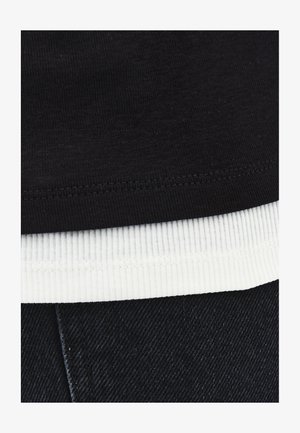 Camiseta de algodón negra con bajo de canalé blanco, combinada con tela de mezclilla oscura; presenta detalles de costura visibles.