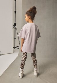 Light purple oversized t-shirt, paired with beige leggings featuring a black leopard print; white sneakers with ankle socks visible.