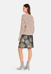 Beige gestrickter Pullover mit strukturierten offenen Mustern, kombiniert mit einem dunklen Blumenrock mit grauen und goldenen Akzenten, und grauen Stiefeletten.