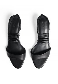 Sandales en cuir noir avec de fines lanières croisées et une large bande à l'orteil. Présente une texture lisse et un design ouvert à l'arrière.