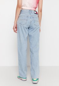 Jeans de mezclilla de tiro alto en azul claro con corte recto, que cuentan con bolsillos traseros y una etiqueta de marca en la cinturilla.