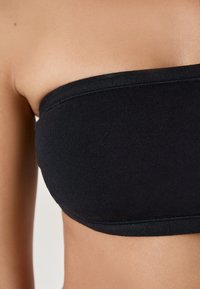 Reggiseno nero senza spalline realizzato in tessuto liscio, caratterizzato da un design senza cuciture e una texture morbida. Nessun abbellimento o motivo presente.