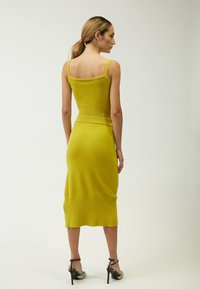 Strick-Midi-Kleid in lebhaftem Gelb mit Spaghetti-Trägern, gerippter Textur und taillierter Silhouette, das direkt unterhalb des Knies endet.