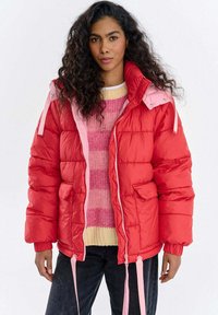 Czerwona puchowa kurtka z różowymi akcentami, z wysokim kołnierzem, zamkiem błyskawicznym i elastycznymi mankietami. Tkanina o teksturze, krój pudełkowy.