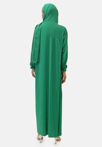 Grünes langes Kleid mit fließendem Design, langen Ärmeln und passendem Kopftuch. Verfügt über elastische Bündchen und eine glatte Stofftextur.