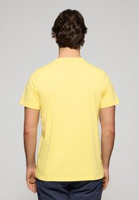 Camiseta amarilla de manga corta con cuello redondo, hecha de suave algodón, con textura lisa y corte recto. Sin patrones ni acentos visibles.