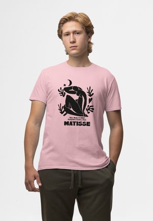 T-shirt in cotone rosa con un design astratto nero di una figura seduta e la scritta "Matisse" in basso. Collo rotondo, maniche corte.