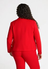 Czerwony marynarkowy żakiet o gładkiej fakturze, z klapami, długimi rękawami i guzikami na mankietach.