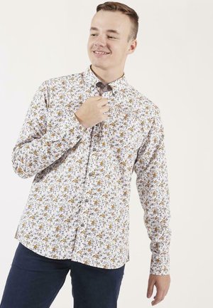 Chemise à boutons, avec un fond blanc, un petit motif floral en jaune et gris, à manches longues, et un col standard. Boutons plus foncés.