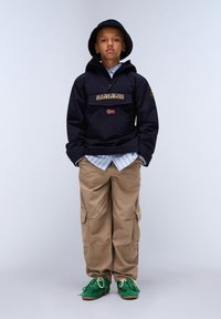 Svart genserjakke med logo-patch, khaki cargo-bukser og grønne sneakers. Utstyret er lagd med en lyseblå stripete skjorte under.